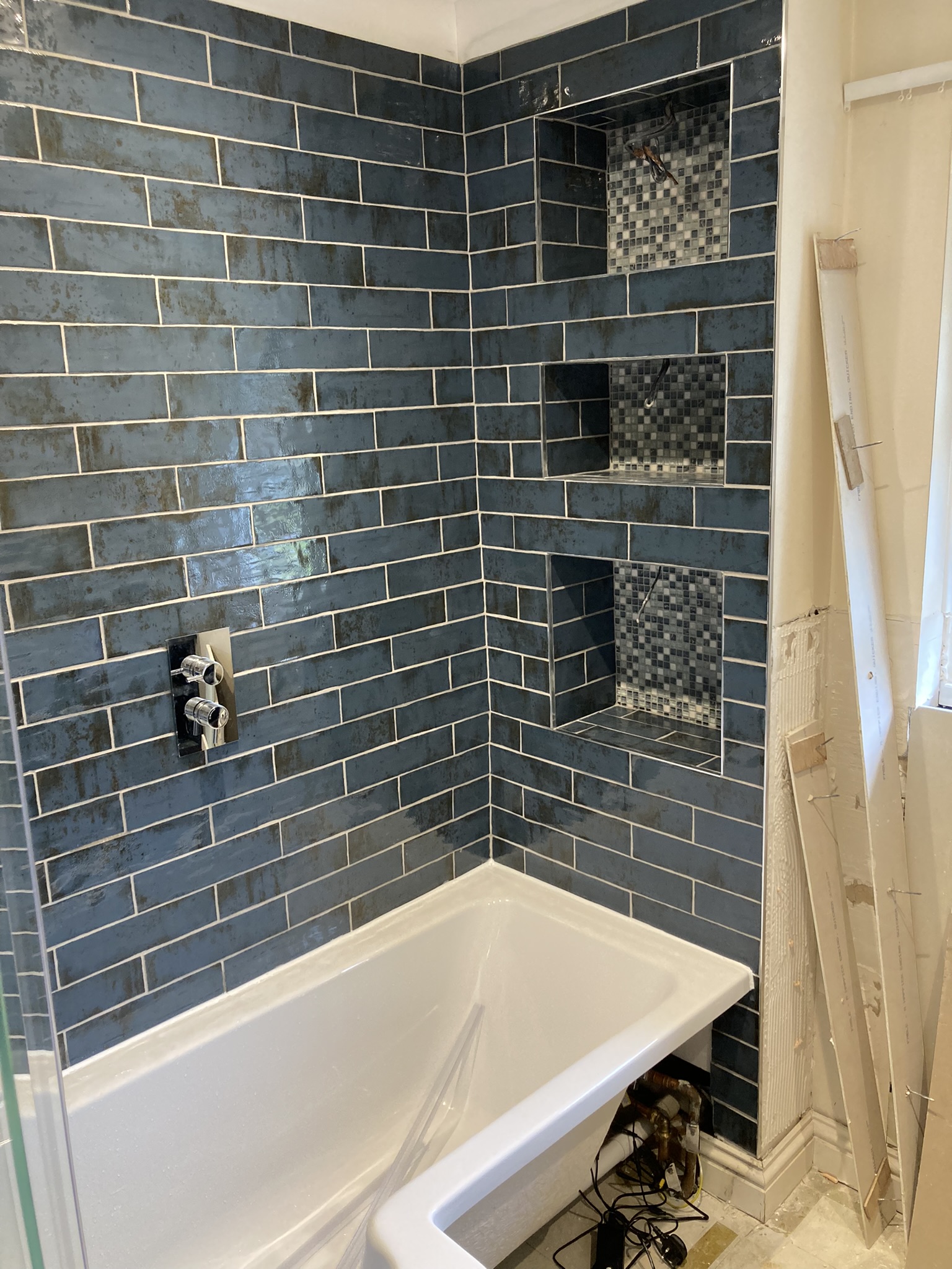 Blue-grey metro tiling over a bath, with mosaic-lined recessed niche shelves and a concealed thermostatic valve.